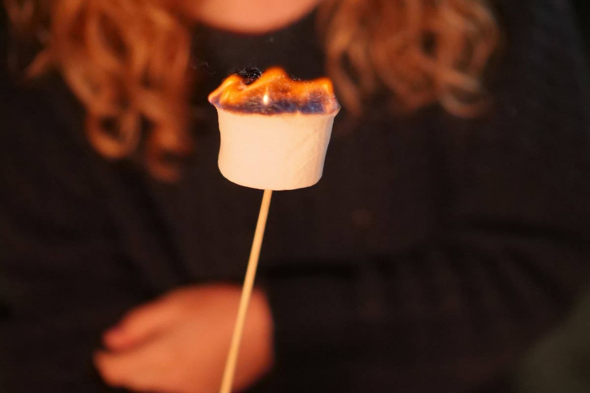 marshmallows-over-a-gas-fire-pit-closing Image of a girls with a roasted marshmallow for a blog post covering roasting marshmallows over a gas fire pit.