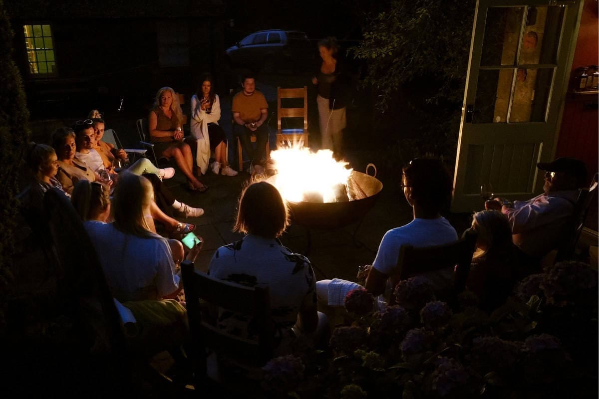 Image of a nightime gathering of a group of people around a large fire pit