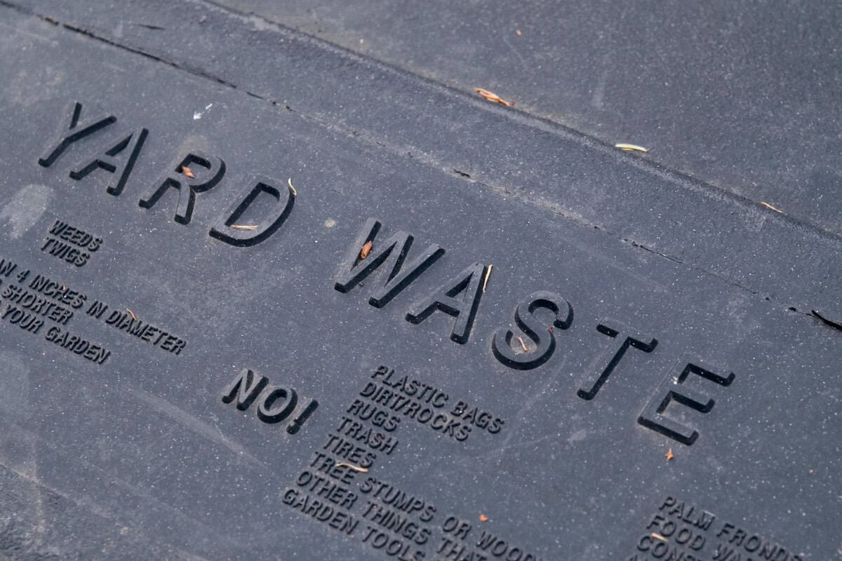 Image of the words "yard waste" on the lid of a waste receptical for a blog post answering the question "is a fire pit open burning?"