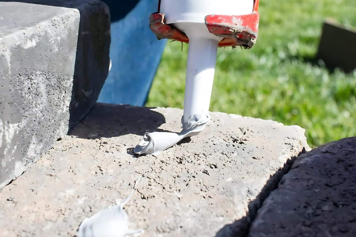 Image of a man applying construction adhesive to a fire pit paver.