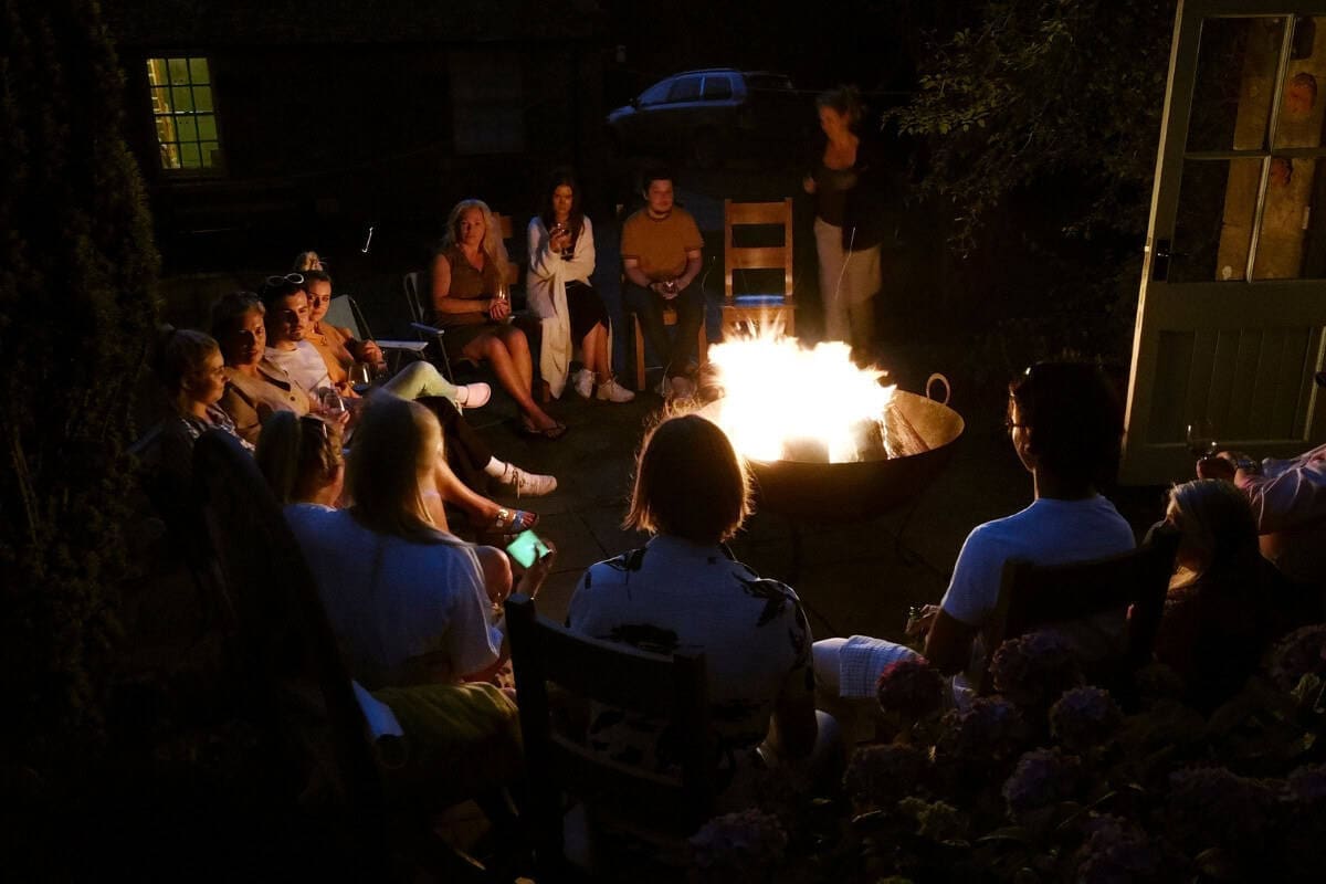 Image a large group of people around a fire pit at night.
