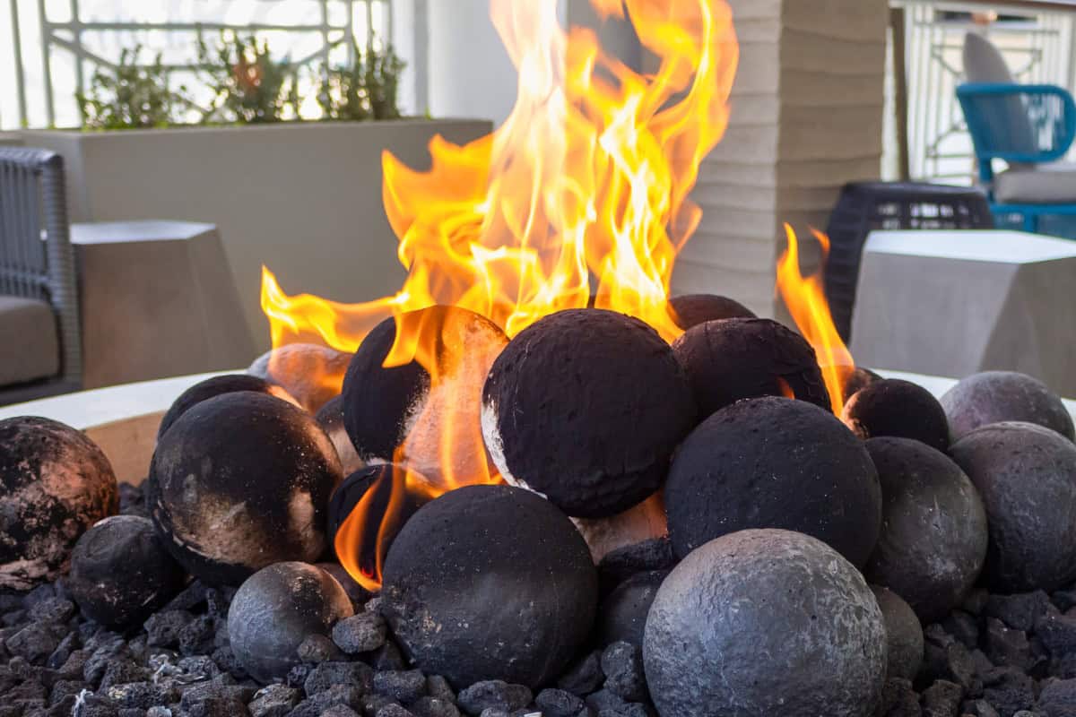 best-fire-pit-fuels-overview Image of rounded fire pit lava rock in a burning gas fire pit.