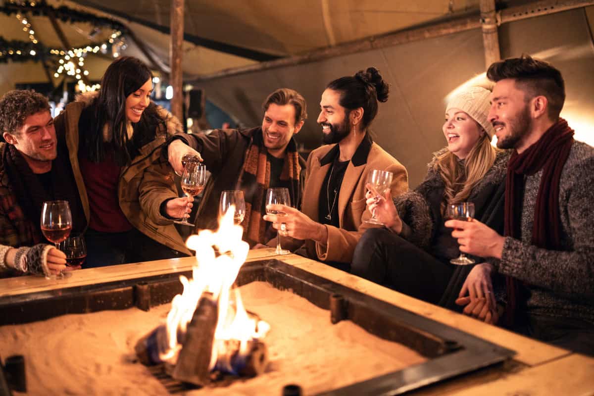 Cozy outdoor fire pit gathering with friends, warm drinks, and holiday decor, perfect for backyard entertaining in fall or winter.