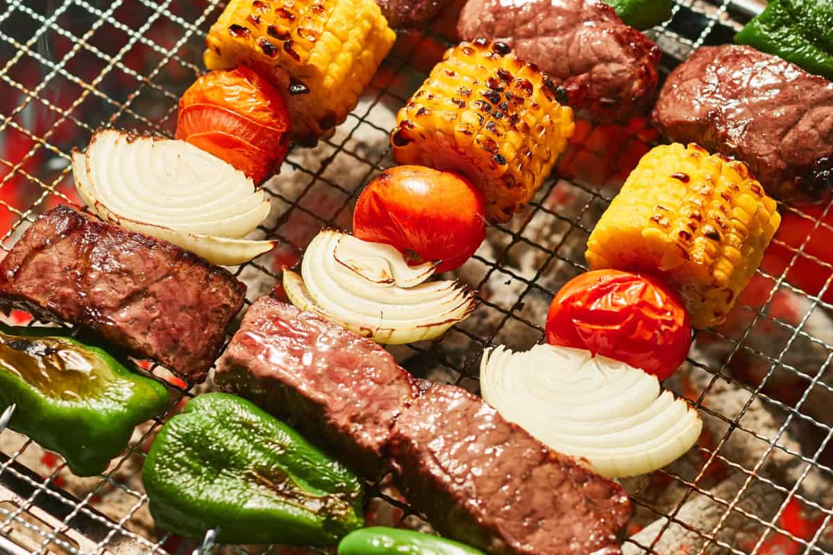 Juicy steaks, grilled vegetables, corn on the cob, cherry tomatoes, and onions sizzling on a backyard grill for outdoor barbecue grilling.