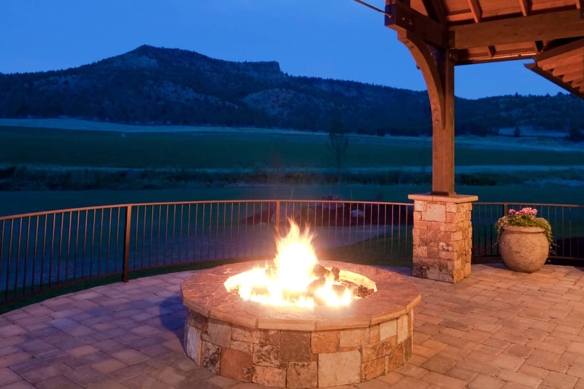 Cozy outdoor fireplace on a scenic mountain landscape porch with stone accents and a potted plant, perfect for backyard gatherings and outdoor entertainment.