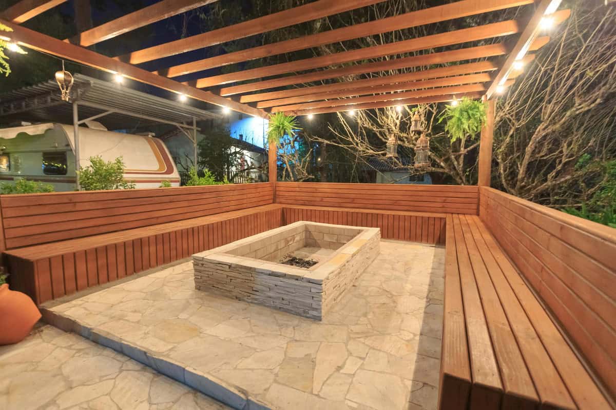 Cozy outdoor backyard fire pit area with wooden seating and string lights at night, perfect for outdoor gatherings and relaxing evenings.