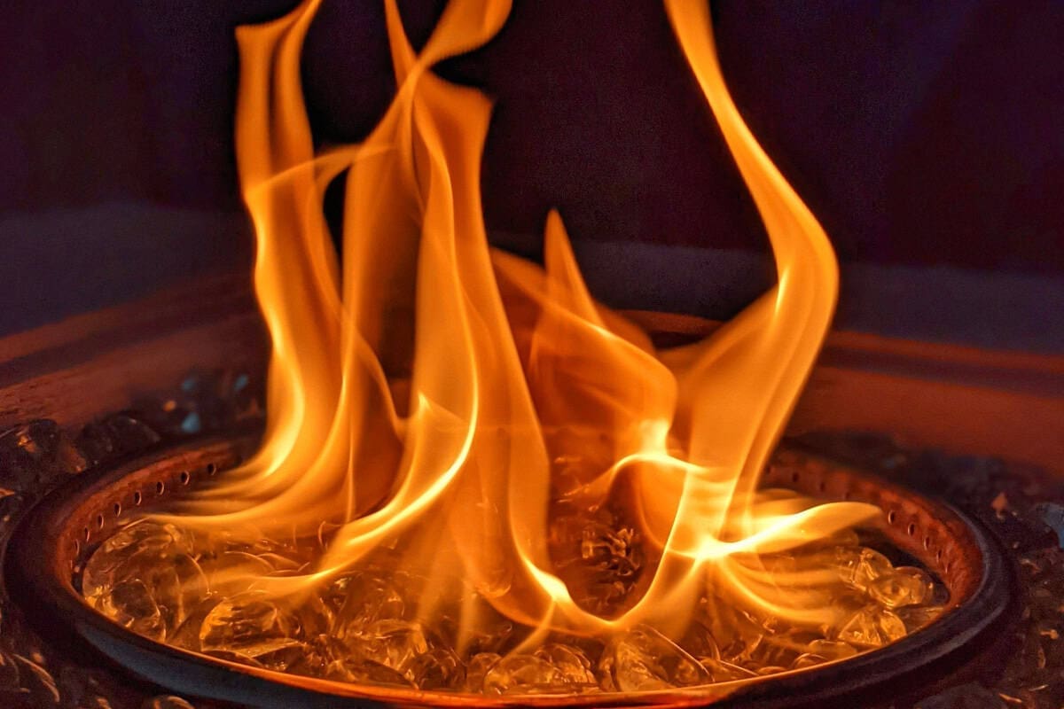 Vivid image of a backyard fire pit with bright orange flames, surrounded by fire glass, creating a cozy outdoor ambiance for relaxing evenings. Perfect for backyard heating and outdoor gatherings.